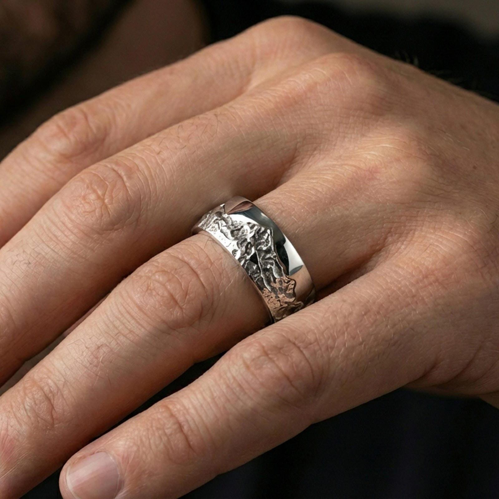 Polished silver mountain scene band ring on finger, crisp terrain engraving and rugged texture, refined everyday wear close-up.