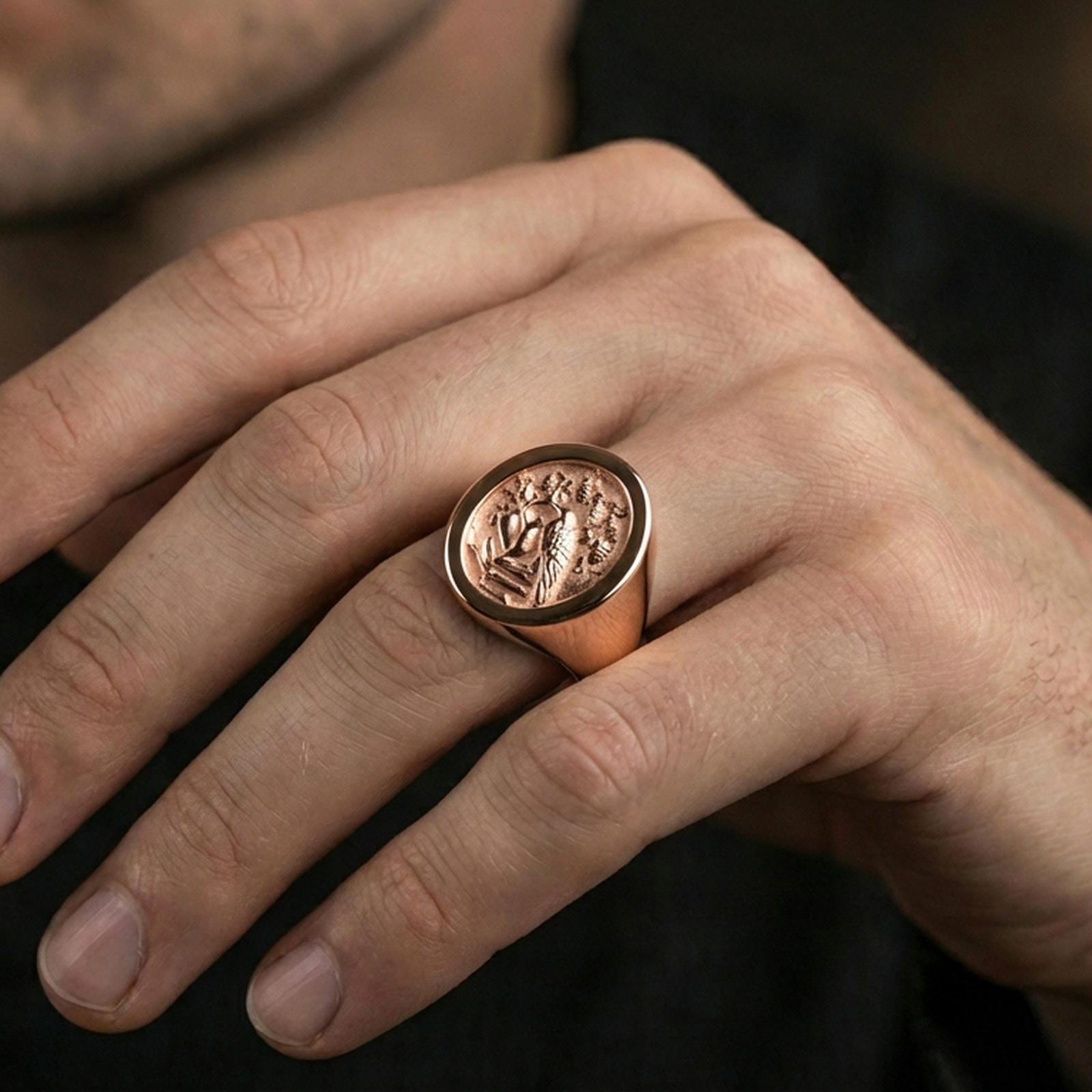 Rose gold plated raven crest signet ring worn on a finger, close-up lifestyle photo showing ornate relief and statement silhouette