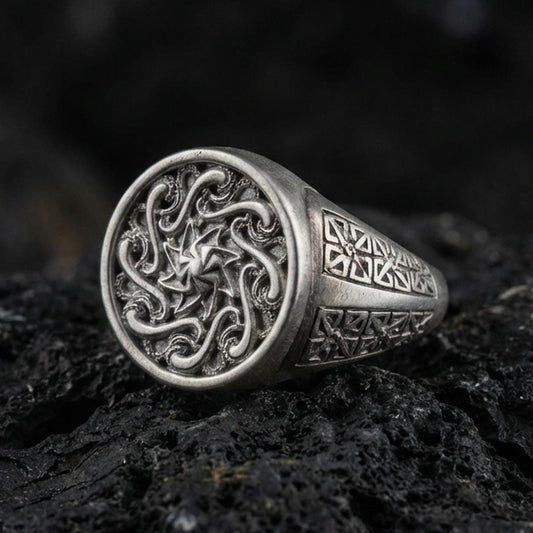 Oxidized sterling silver spiral sun signet ring with swirling Celtic-style face and geometric side panels, macro shot on black volcanic rock