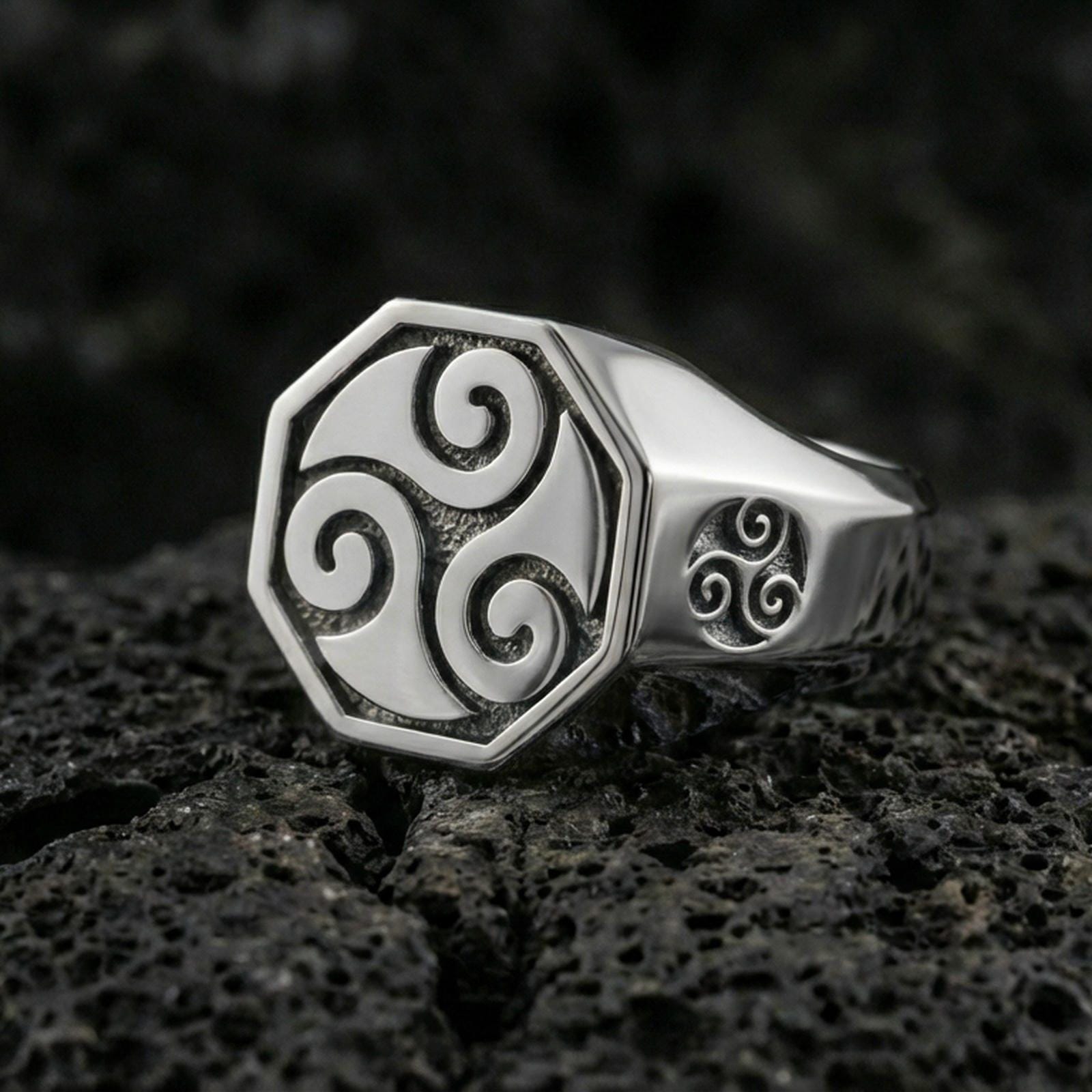 Polished silver octagonal signet ring featuring a bold Celtic triskelion symbol and side swirl detail, close-up product shot on volcanic stone