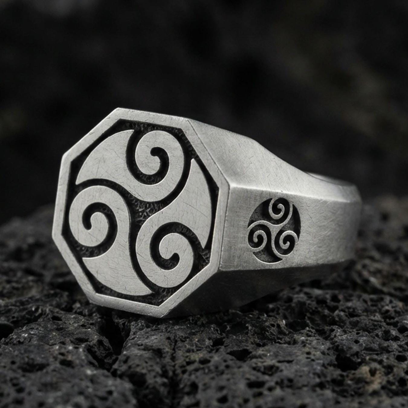 Oxidized sterling silver octagon signet ring with Celtic triskelion swirl engraving and matching side emblem, macro photo on black volcanic rock