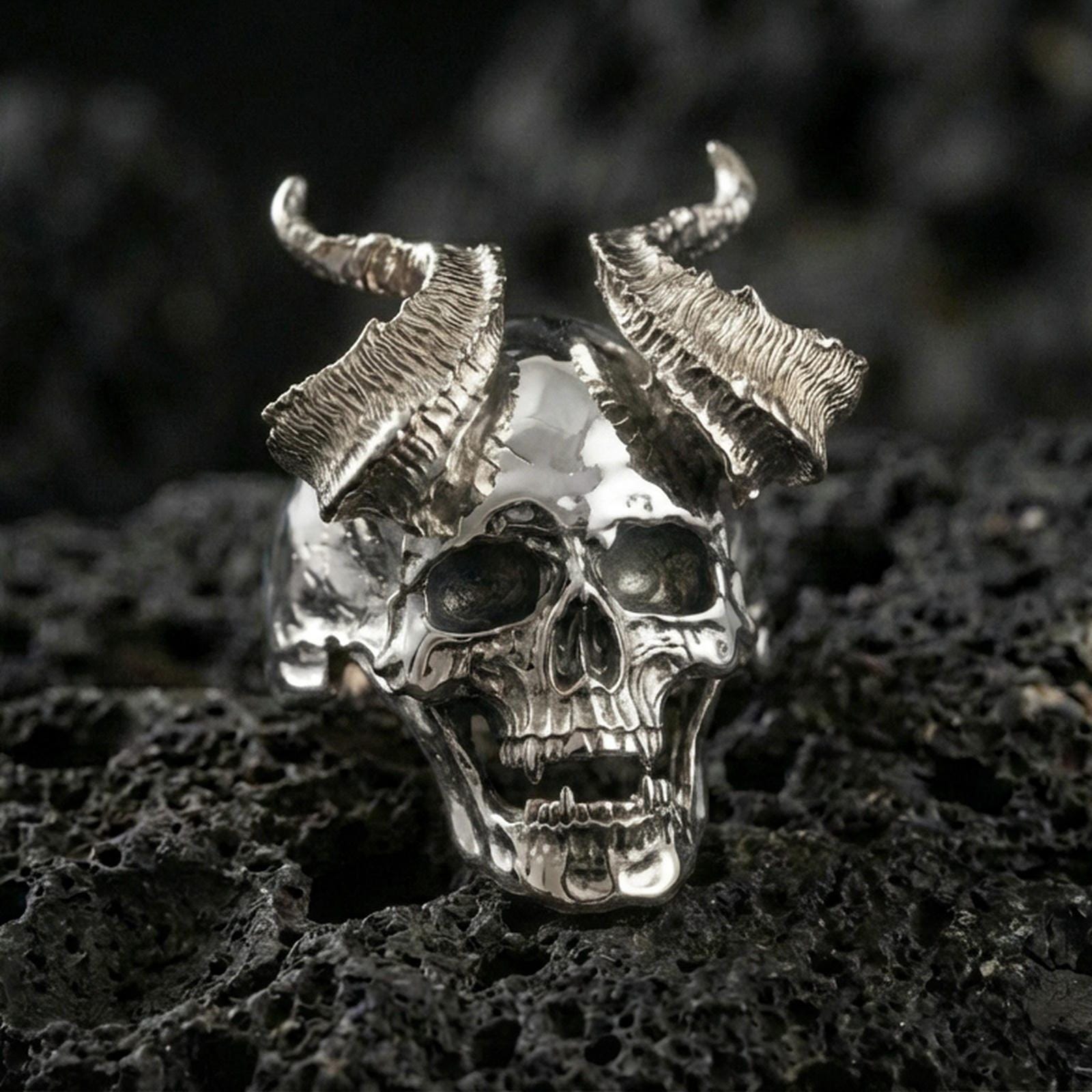 Polished silver horned skull ring featuring high-relief teeth and textured horn segments, close-up product shot on volcanic stone