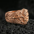 Load image into Gallery viewer, Rose gold plated fleur-de-lis ring with ornate botanical scrolls and vintage-style texture, close-up photo on volcanic rock
