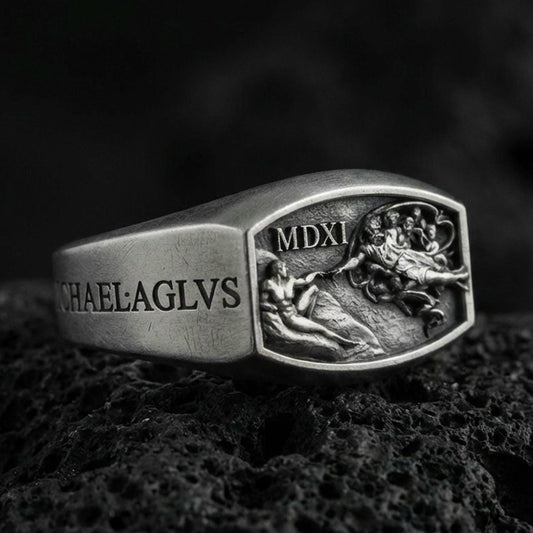 Oxidized sterling silver Archangel Michael ring with MDXI engraving and battle relief panel, macro product photo on black volcanic rock