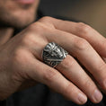 Load image into Gallery viewer, Oxidized devil face signet ring worn on a finger, lifestyle close-up highlighting the crossed blades and deep relief details
