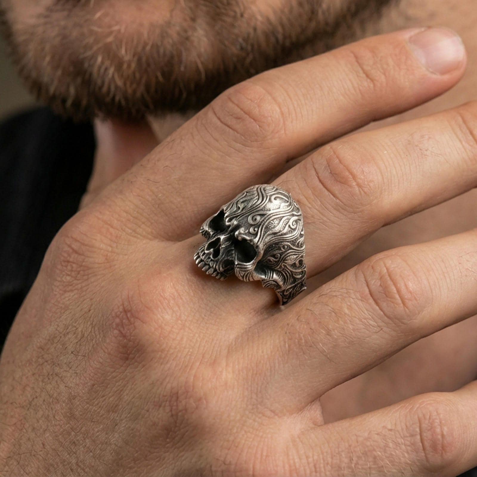 Oxidized baroque skull ring worn on a finger, lifestyle close-up emphasizing the engraved scroll texture and darkened recesses
