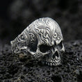 Load image into Gallery viewer, Oxidized sterling silver skull ring with baroque scroll engravings and deep shadowed relief, macro product photo on black volcanic rock
