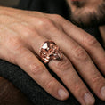 Load image into Gallery viewer, Rose gold plated skull ring on a finger, lifestyle shot focusing on the sleek skull profile and deep shadowed eye sockets
