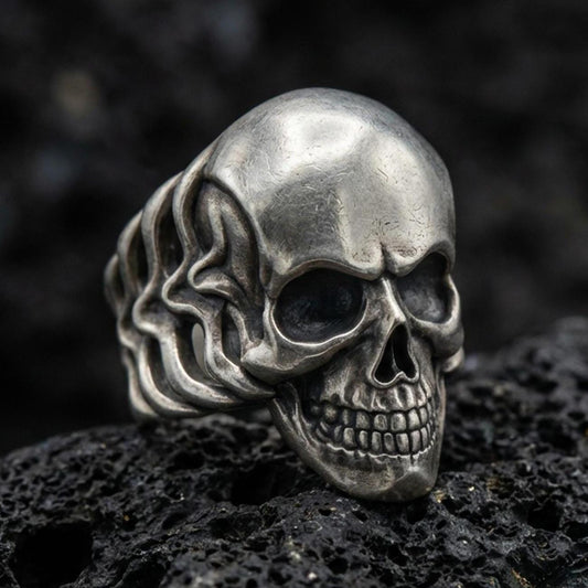 Oxidized sterling silver skull ring with smooth dome forehead and deep blackened eye sockets, macro product photo on black volcanic rock