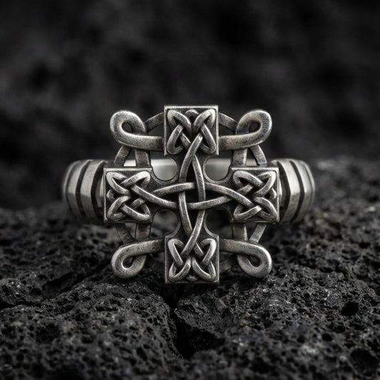Oxidized sterling silver Celtic knot cross ring with interlaced Trinity-style weave and darkened recessed texture, macro product photo on black volcanic rock