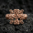 Load image into Gallery viewer, Rose gold plated Celtic knot cross ring with intricate interlace pattern and sculpted cross silhouette, close-up on volcanic rock
