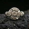 Load image into Gallery viewer, Polished silver Celtic windflower ring featuring a sculpted flower swirl center and Celtic knotwork petals, close-up on volcanic stone
