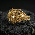 Load image into Gallery viewer, Gold plated double skull motorcycle ring with sculpted handlebar motif and layered chain texture, product-only macro image on black volcanic rock
