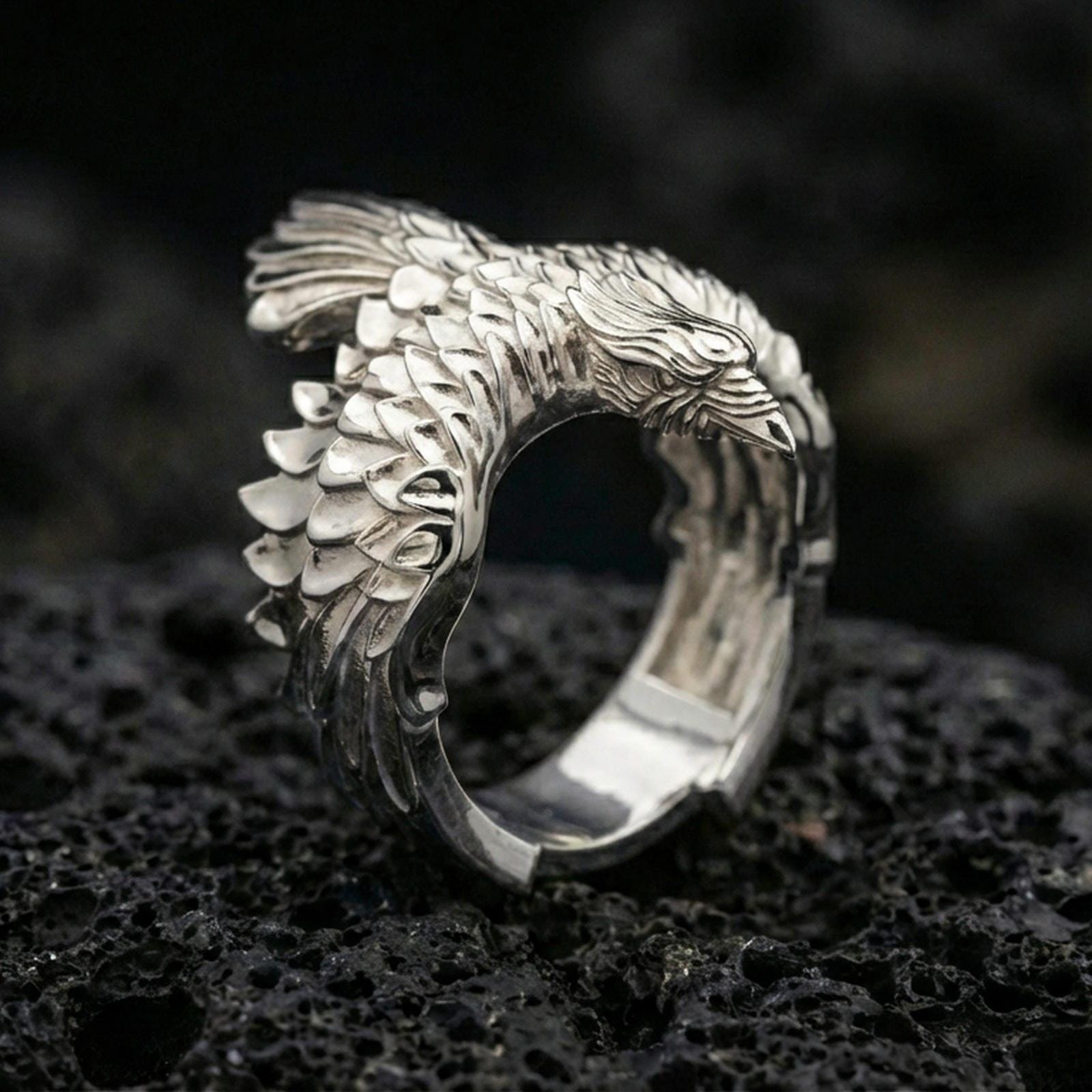 Polished silver adjustable wing ring featuring detailed feathers and a raptor head tip, close-up product shot on volcanic stone