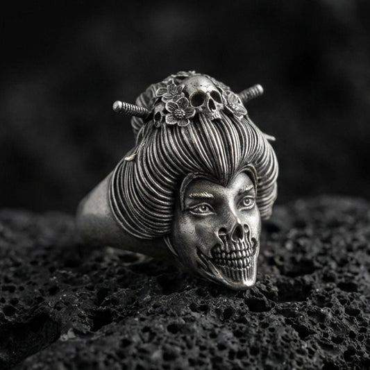 Oxidized sterling silver geisha skull ring with detailed hair bun, floral ornaments, and skeletal jaw, macro product photo on black volcanic rock