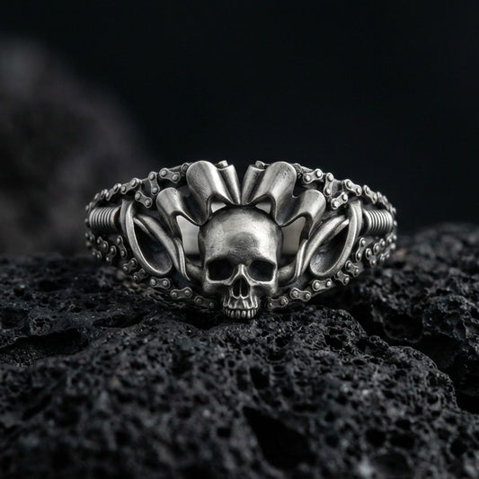 Oxidized sterling silver skull ring with crown-like spikes and chain-link band details, macro product photo on black volcanic rock