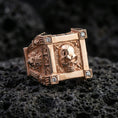 Load image into Gallery viewer, Rose gold plated skull ring with square bezel-style frame, raised skull centerpiece, and lab diamond corners, close-up on black volcanic rock
