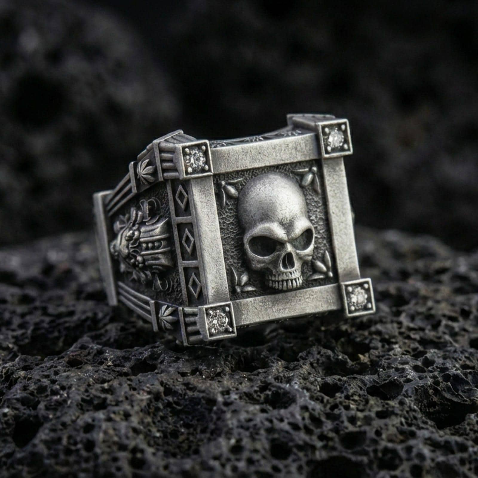 Oxidized sterling silver skull ring with square frame setting and lab diamond accents, macro product photo on black volcanic rock