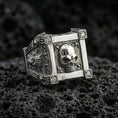 Load image into Gallery viewer, Polished silver skull ring featuring a framed skull centerpiece and lab diamond corner details, close-up on volcanic stone
