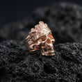 Load image into Gallery viewer, Rose gold plated skull ring with tree bark texture carving and engraved band motifs, close-up on black volcanic rock
