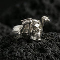 Load image into Gallery viewer, Polished silver skull biker ring featuring aviator goggles and sculpted skeleton arms, close-up on volcanic stone
