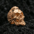 Load image into Gallery viewer, Rose gold plated bearded skull ring with high-relief hair and beard detailing, close-up on volcanic rock
