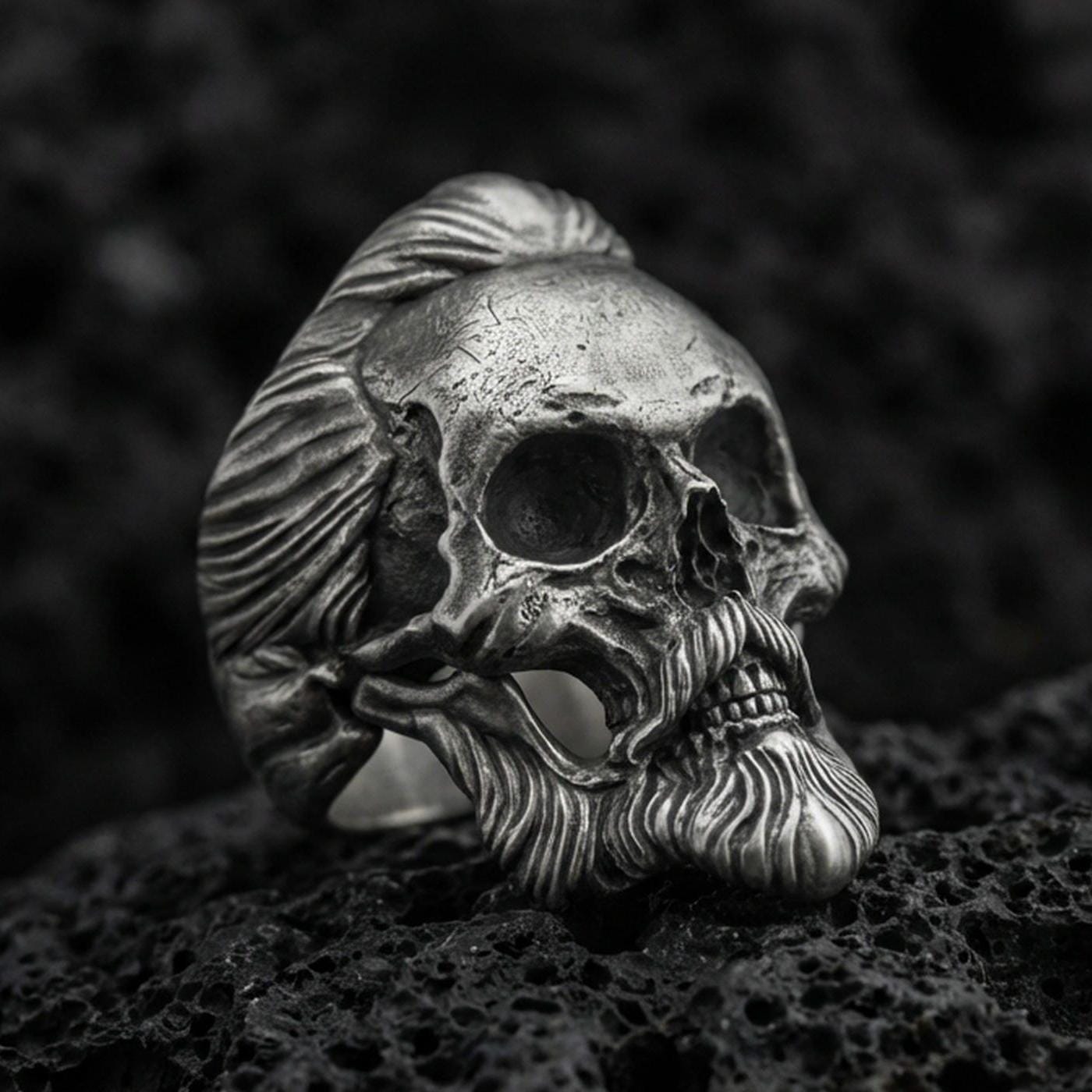 Oxidized sterling silver skull ring with sculpted beard and swept-back hair, macro product photo on black volcanic rock