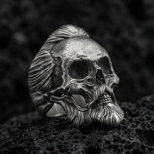 Oxidized sterling silver skull ring with sculpted beard and swept-back hair, macro product photo on black volcanic rock