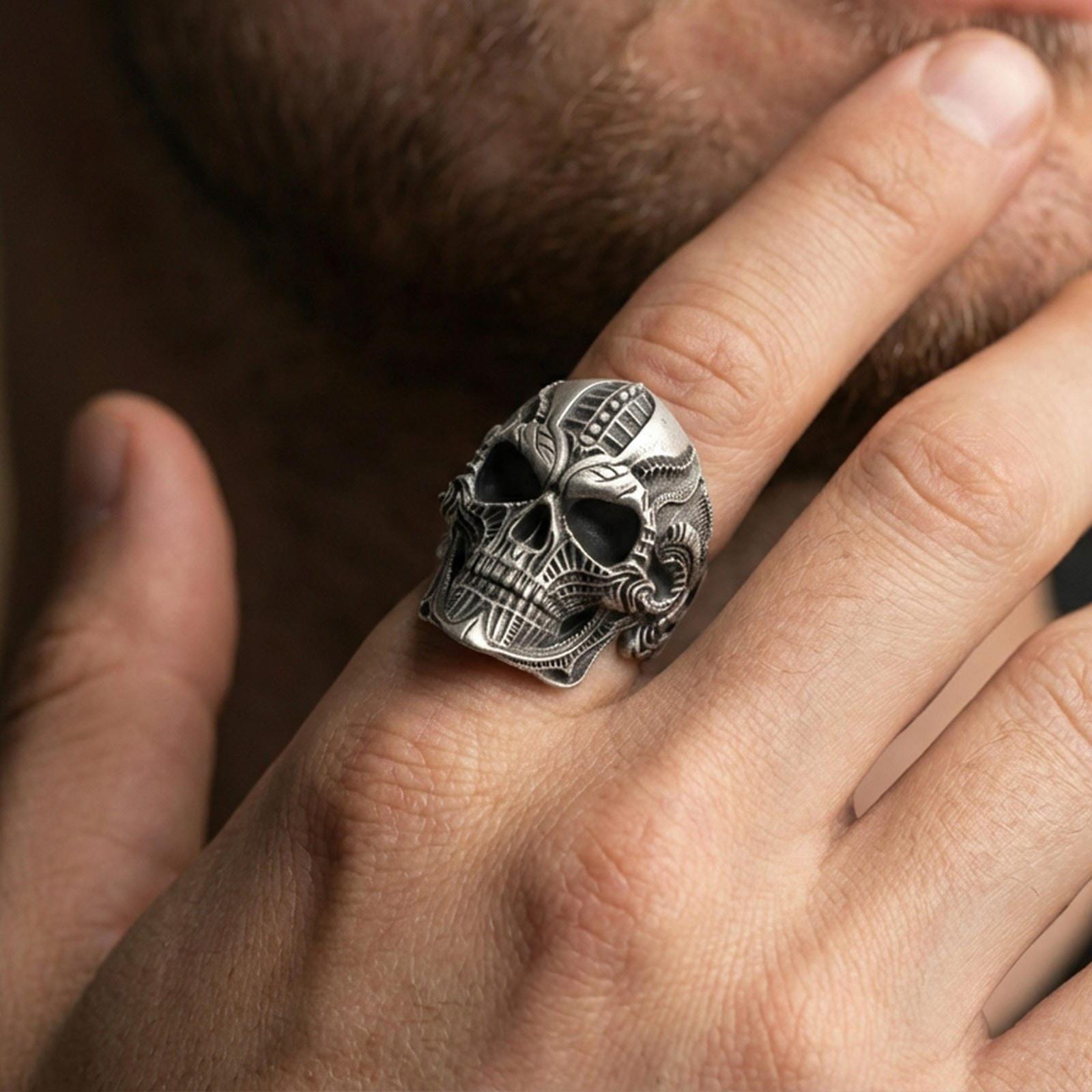 Oxidized biomechanical skull ring worn on a finger, close-up lifestyle shot highlighting the sci-fi engraved skull face