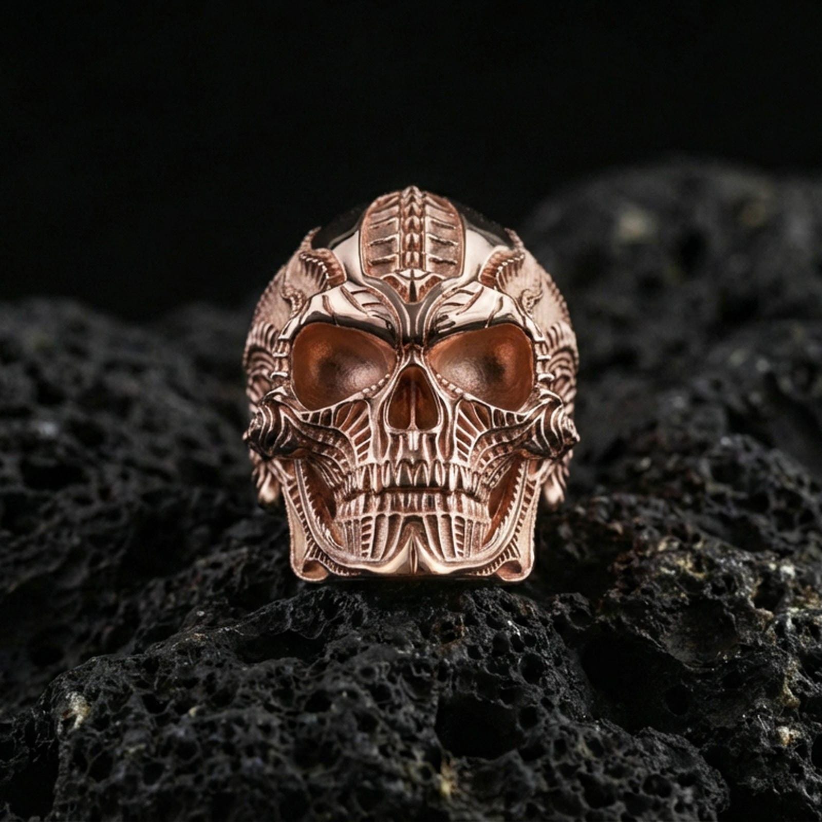 Rose gold plated cyber skull ring with futuristic mechanical engraving and high-contrast skull relief, close-up on volcanic rock