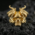 Load image into Gallery viewer, Gold plated horned skull ring featuring raised skull relief and rugged horn texture, product-only macro on black volcanic rock

