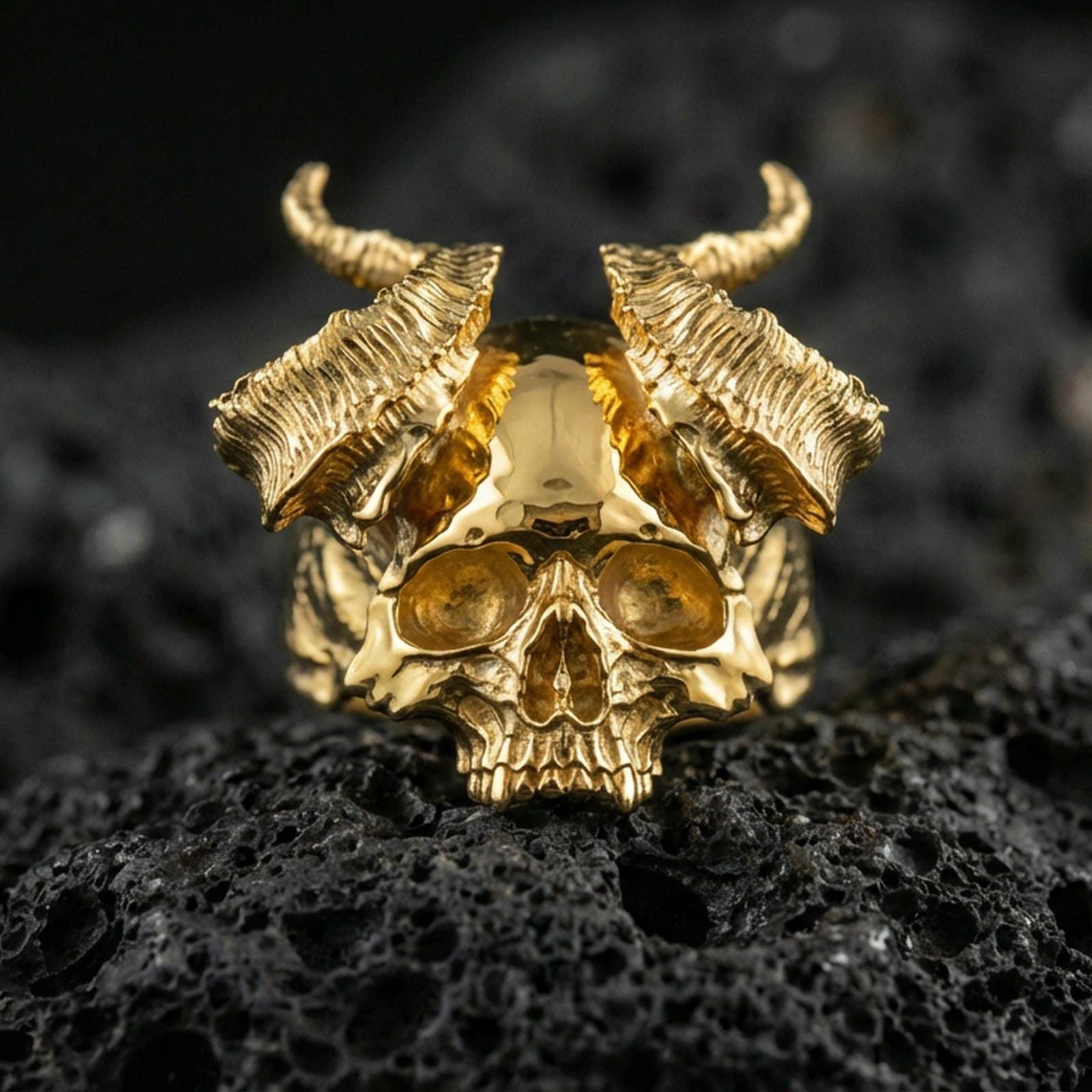 Gold plated horned skull ring featuring raised skull relief and rugged horn texture, product-only macro on black volcanic rock