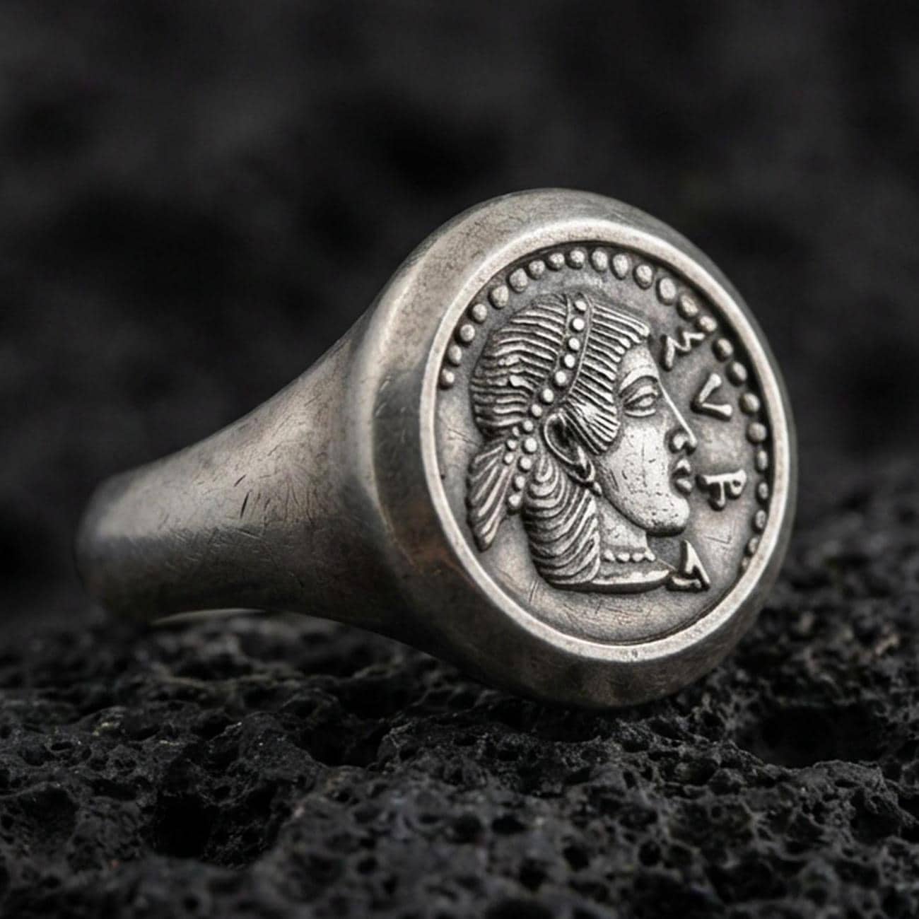 Oxidized sterling silver Greek coin signet ring with a classical female profile and dotted border, macro photo on black volcanic rock