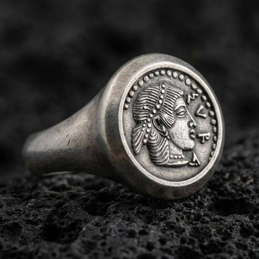 Oxidized sterling silver Greek coin signet ring with a classical female profile and dotted border, macro photo on black volcanic rock