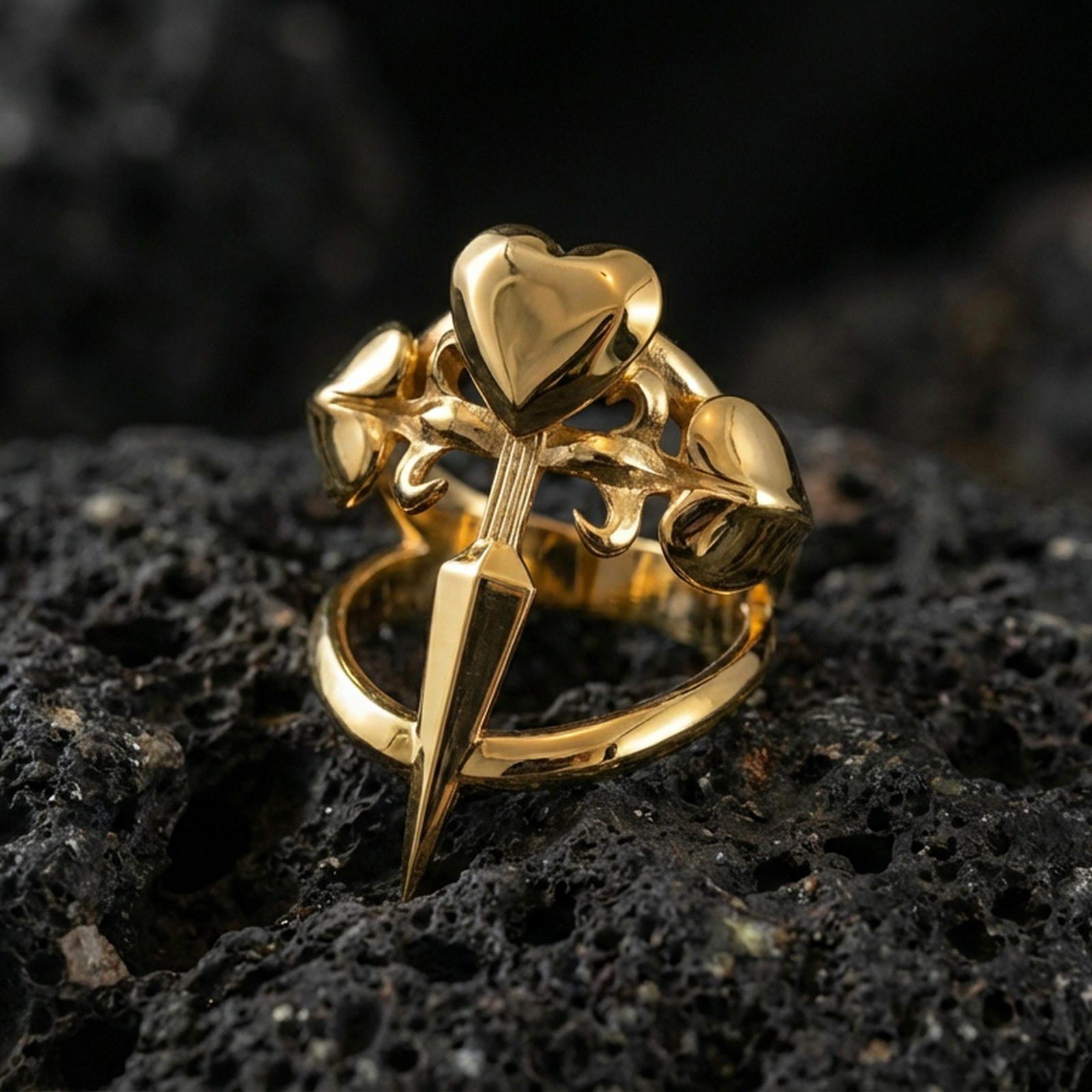 Gold plated heart dagger ring with a sharp dagger silhouette and heart-shaped top detail, product-only macro on black volcanic rock