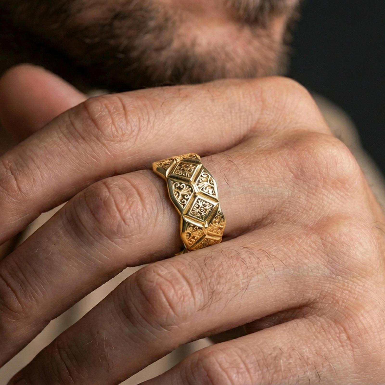 Gold plated engraved ornament band worn on finger, raised diamond pattern with scrollwork accents, premium lifestyle jewelry photo.
