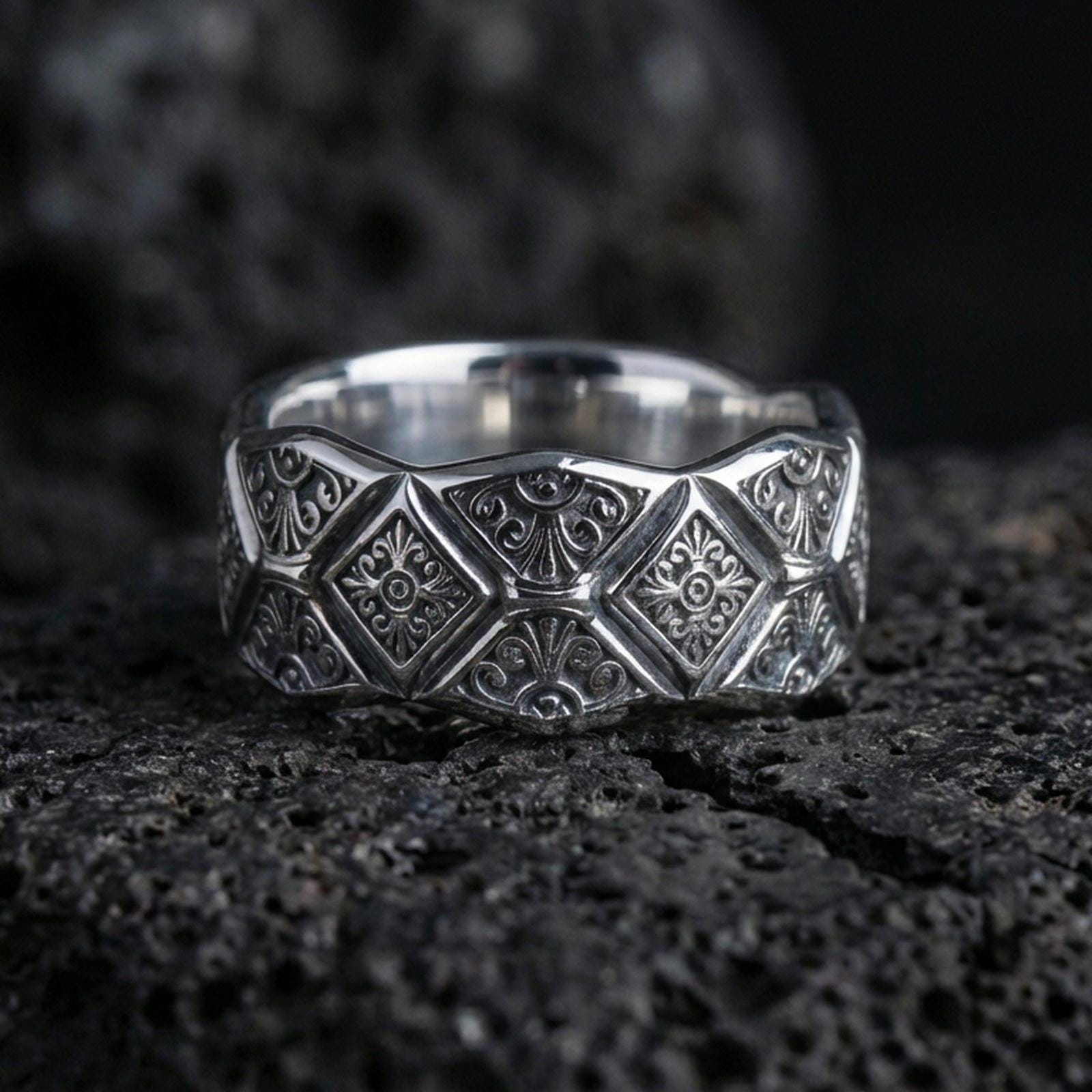 Polished silver engraved geometric band ring on black volcanic stone, crisp diamond motifs and ornate filigree engraving, centered close-up studio lighting.