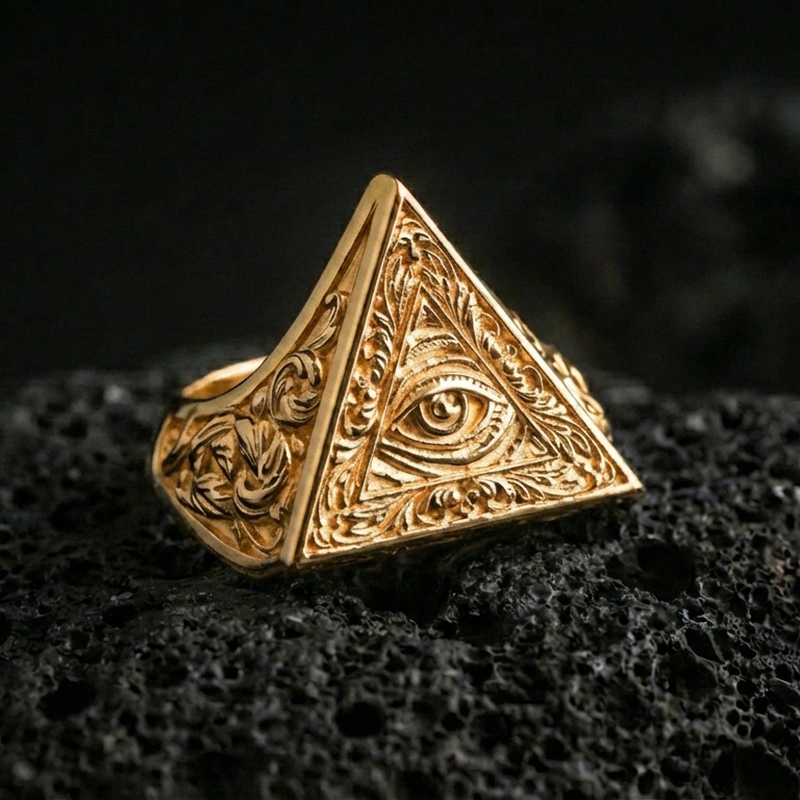 Gold plated all-seeing eye triangle ring with detailed filigree engravings and bold signet profile, macro photo on black volcanic rock