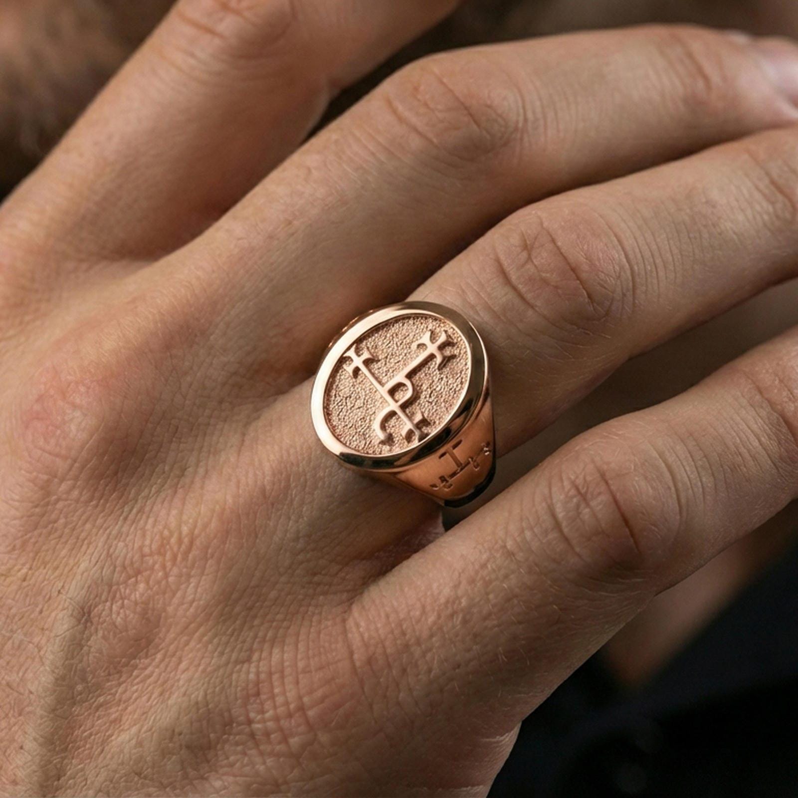 Rose gold plated oval signet ring worn on the finger, close-up lifestyle image focusing on the textured face and sigil design