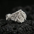 Load image into Gallery viewer, Polished silver Freemason ring featuring the square and compass symbol with raised “G” and detailed engraving, macro on volcanic stone
