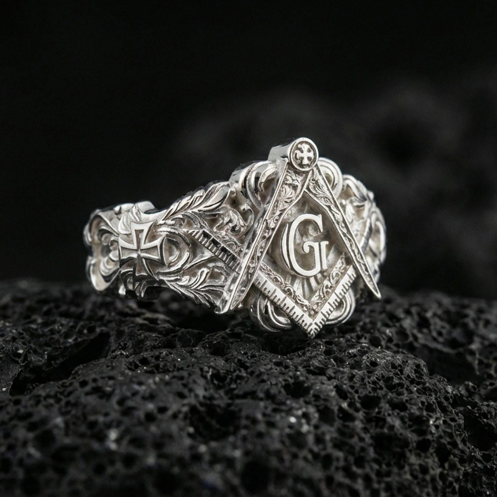 Polished silver Freemason ring featuring the square and compass symbol with raised “G” and detailed engraving, macro on volcanic stone