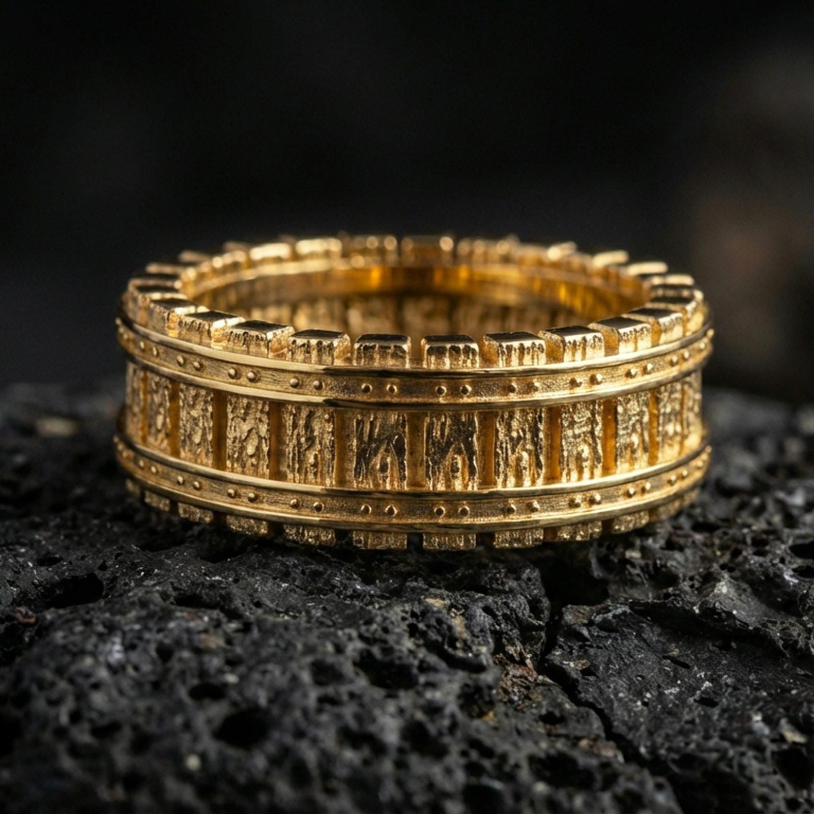 Gold plated railway track band ring on volcanic rock, detailed riveted borders with rugged mechanical texture, luxury jewelry product photography.