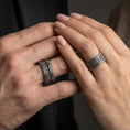 Load image into Gallery viewer, Oxidized sterling silver railway track band worn on finger, industrial rivet lines and rugged texture detail, natural lifestyle hand shot with shallow depth of field.
