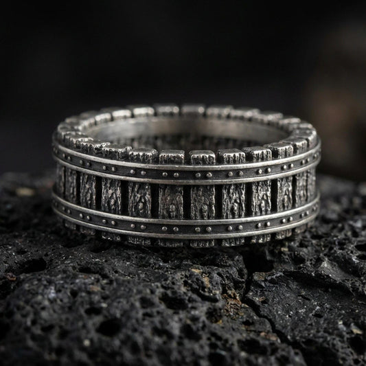 Oxidized sterling silver railway track band ring on dark volcanic rock, industrial rivet lines and train rail texture, premium macro product shot.