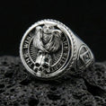 Load image into Gallery viewer, Polished silver signet ring featuring a detailed owl perched above a skull motif with engraved quote border, macro on volcanic stone
