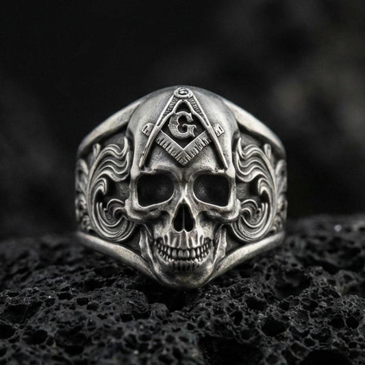 Oxidized sterling silver Masonic skull ring with compass-and-G emblem and engraved scrollwork, on black volcanic rock