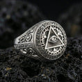 Load image into Gallery viewer, Polished silver Masonic eye-in-triangle signet ring with circular Latin motto border and ornate side engraving, on volcanic stone
