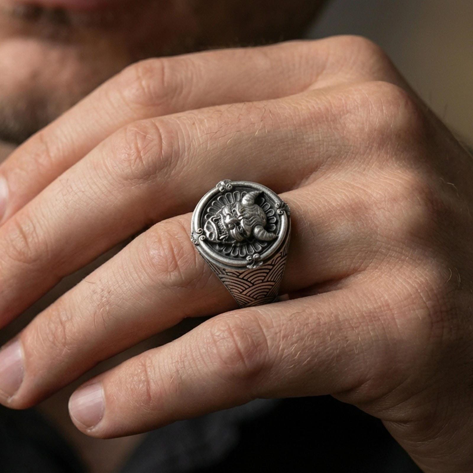 Oxidized seigaiha wave oni mask ring worn on a finger, close-up lifestyle shot highlighting the horned demon face and engraved pattern
