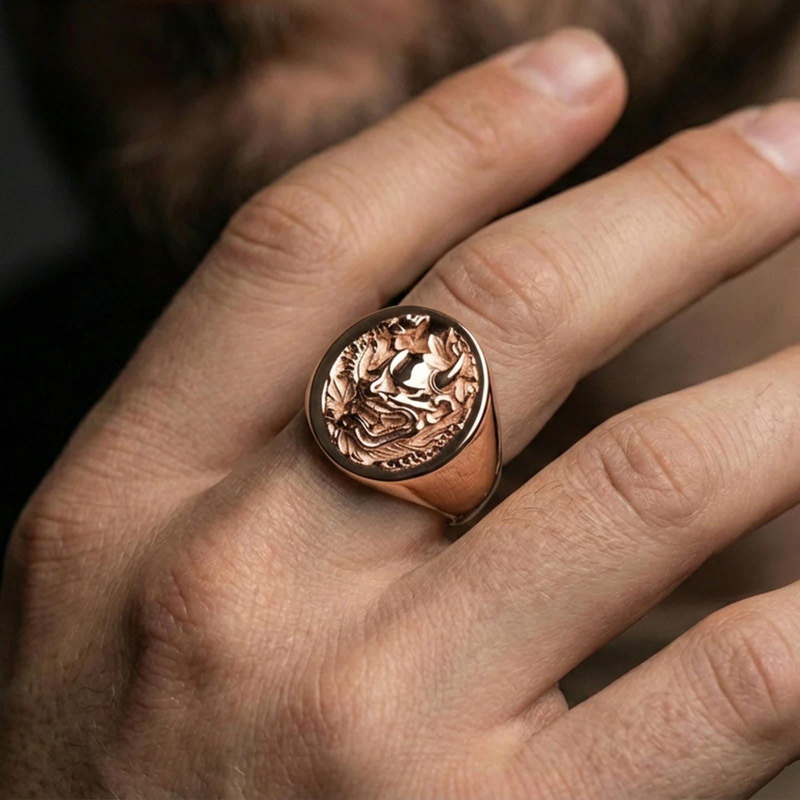 Rose gold plated Japanese oni demon ring worn on a finger, macro lifestyle image showcasing the relief carving and floral motif