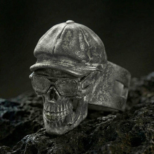 Sterling silver skull ring with an oxidized finish, wearing a vintage cap and glasses, macro on black volcanic rock